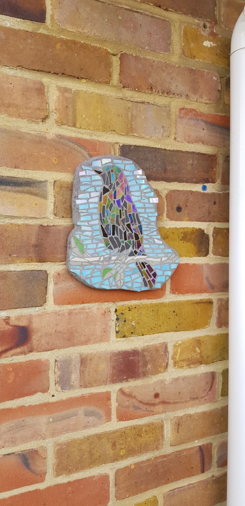 Wall plaque featuring a crow sitting on a branch. The background is blue to simulate the sky.