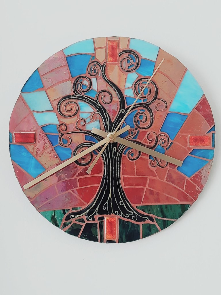 A clock made of coloured glass and wood depicting red sunrise against a blue sky background.