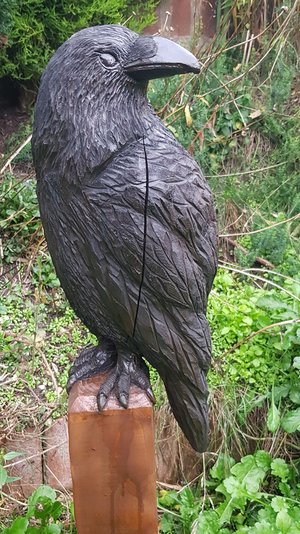 The Crow - wooden carving in black. The crow sits on a pedestal of natural wood.
