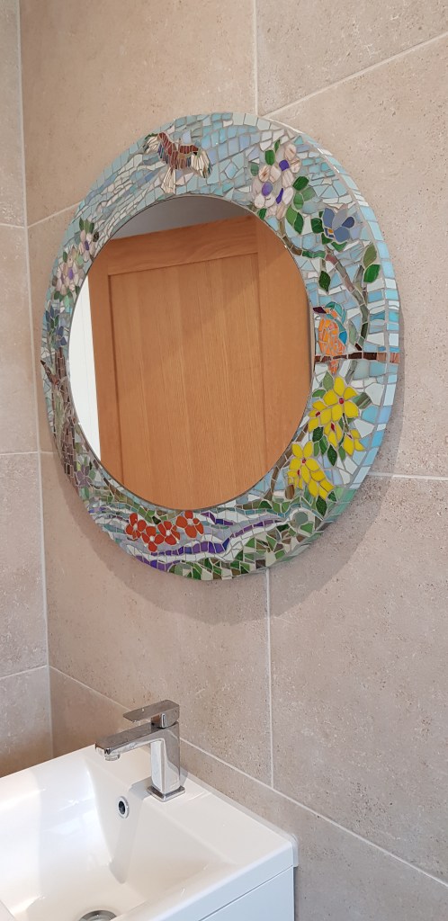 Bathroom mirror with a wider border, decorated with flora and forna, blue skies and a trickling stream.