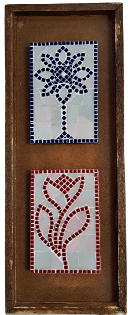 Two small pieces of mosaic art are situated in a dark-stained wooden frame. The mosaics represent flowers and use whole micro-tesserae to draw the outlines of the flowers while leaving the backgrounds in larger plain but iridescent tiles.
